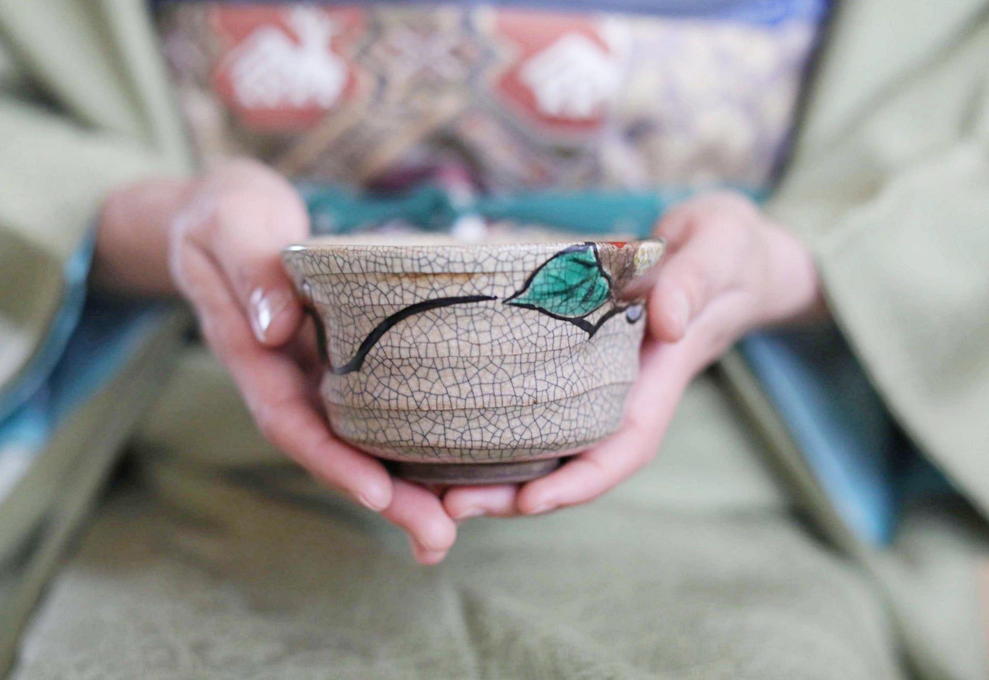 A person's hands holding a ceramic bowl with a green leaf design.