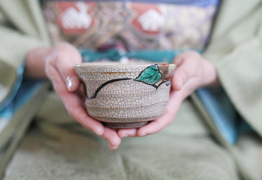 A person's hands holding a ceramic bowl with a green leaf design.