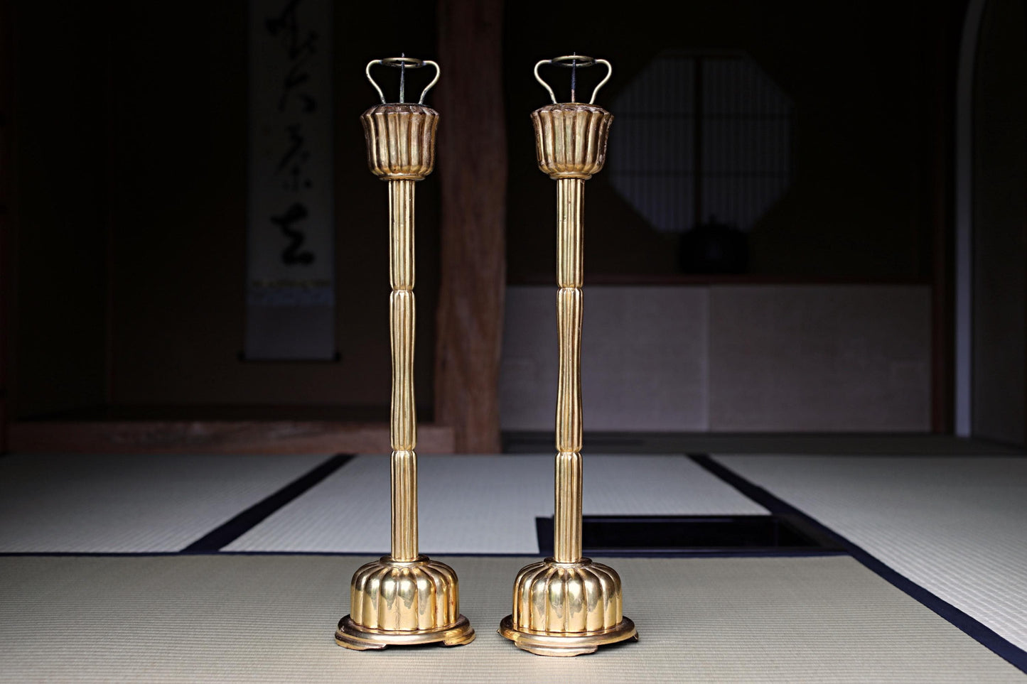 two golden candlesticks standing side by side on a tatami mat.