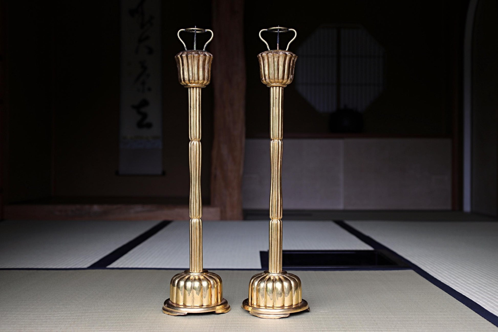 two golden candlesticks standing side by side on a tatami mat.