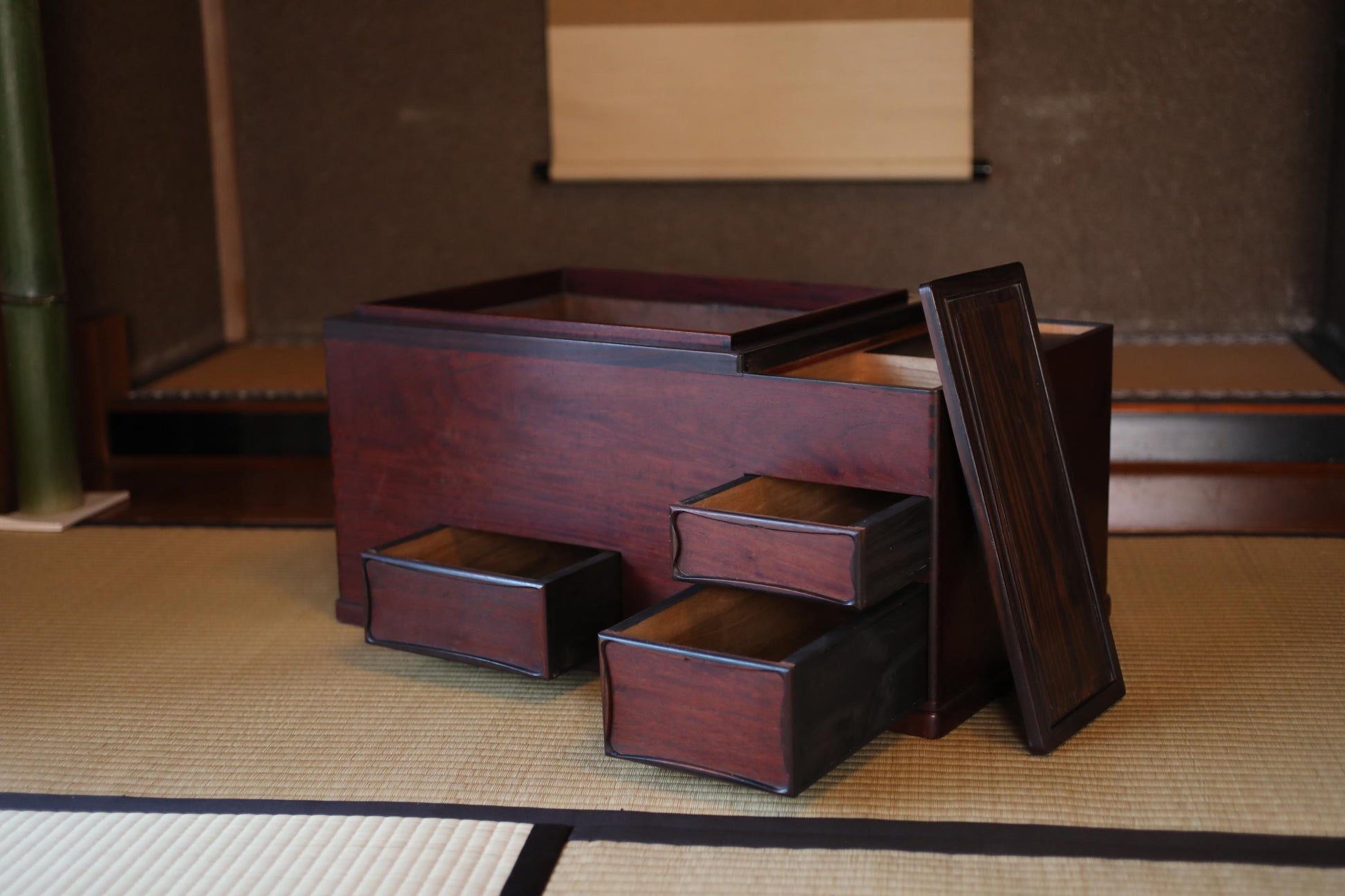 A wooden chest with four drawers sits on a tatami mat in a room with a bamboo wall.