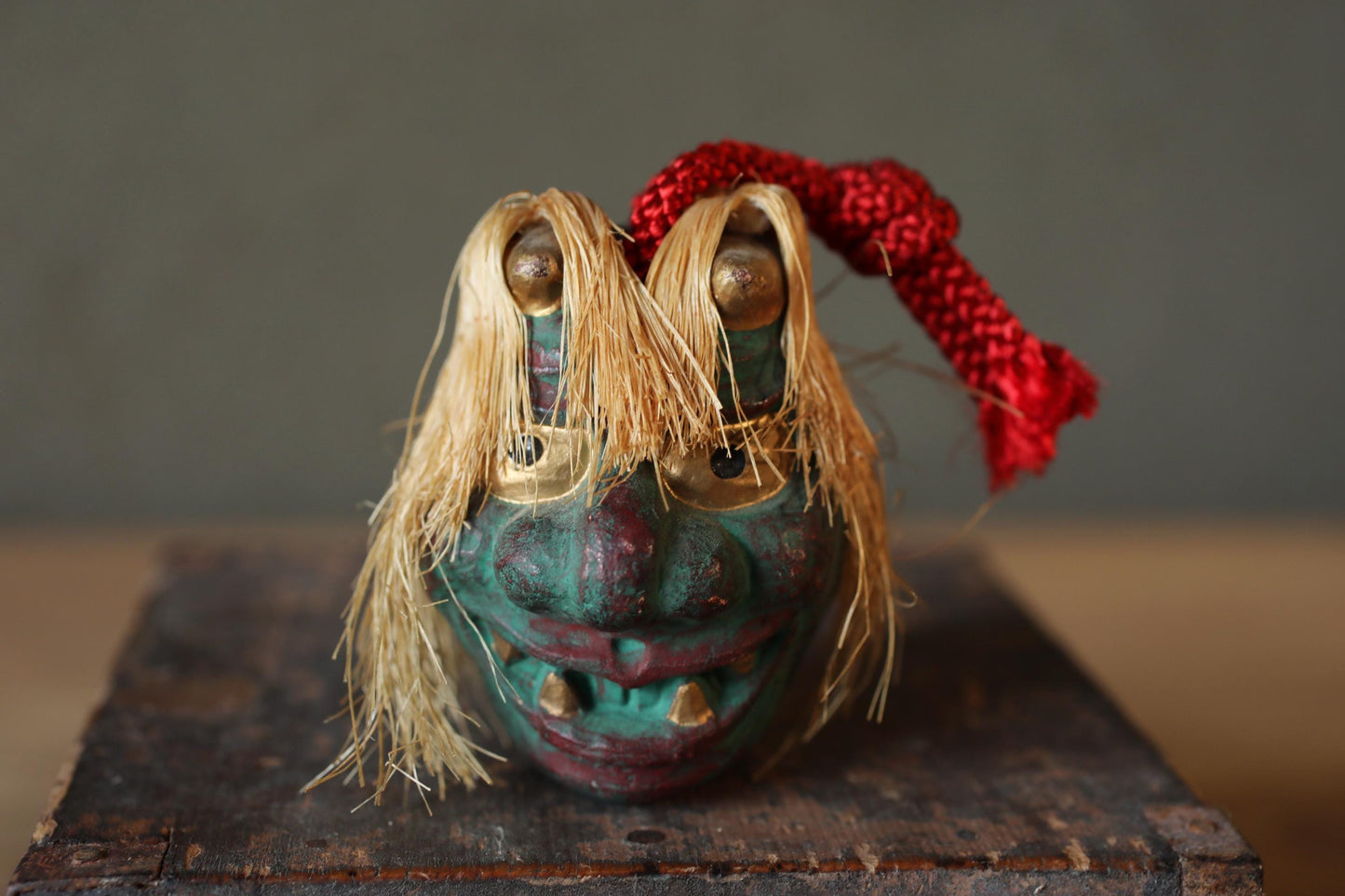 A colorful, whimsical mask with a red ribbon tied around it, sitting on a wooden surface.