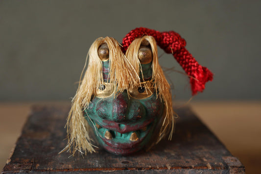 A colorful, whimsical mask with a red ribbon tied around it, sitting on a wooden surface.
