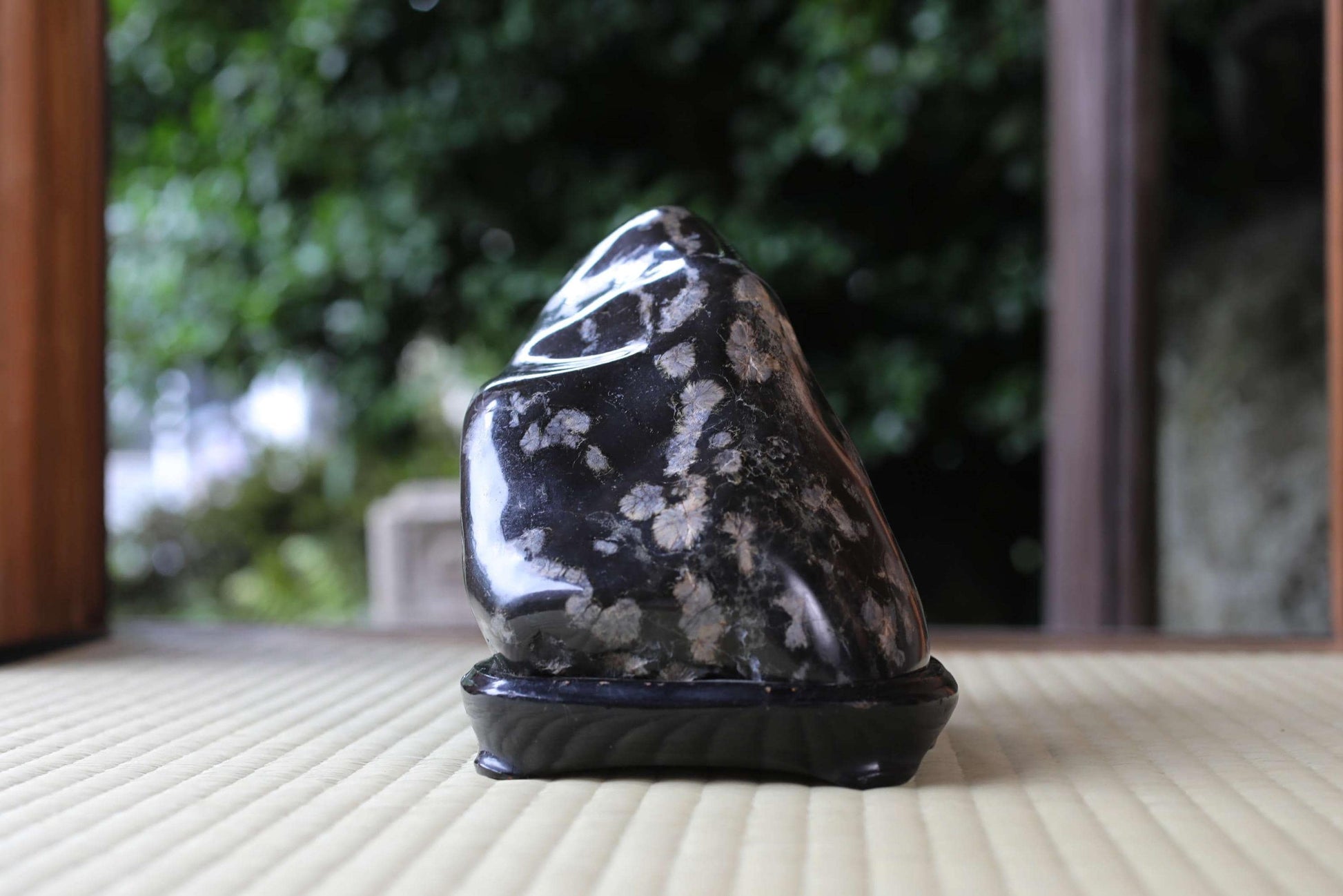 A black and white speckled rock sits on a black stand, placed on a beige surface.