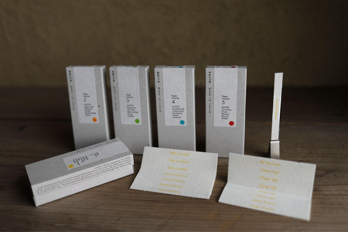 a collection of five white boxes with text on them, arranged on a wooden surface. There are also two white business cards with text on them, placed next to the boxes.