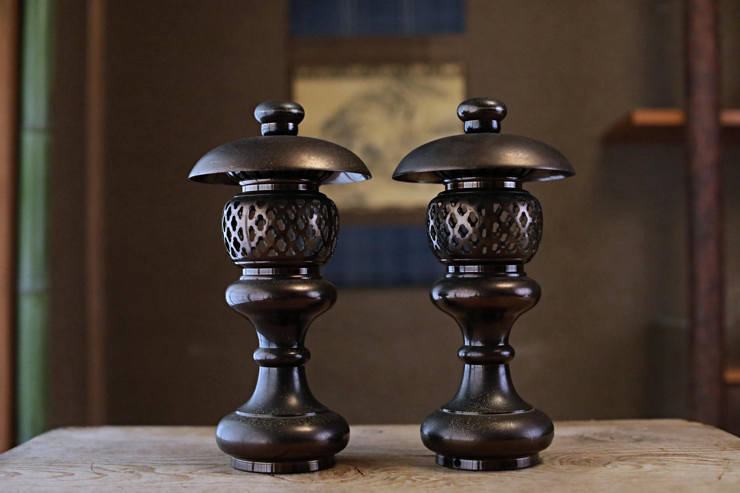 Two ornate, black metal lanterns with intricate designs stand side by side on a wooden surface.