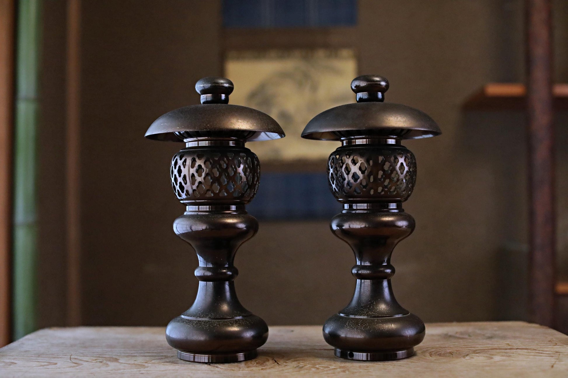 Two ornate, black metal lanterns with intricate designs stand side by side on a wooden surface.