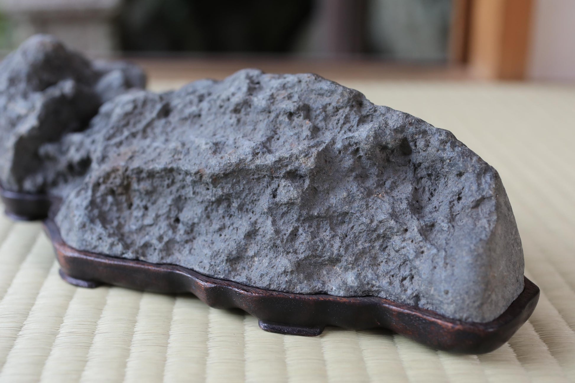 A close-up image of a large, gray rock with a rough, textured surface, resting on a wooden stand or base.