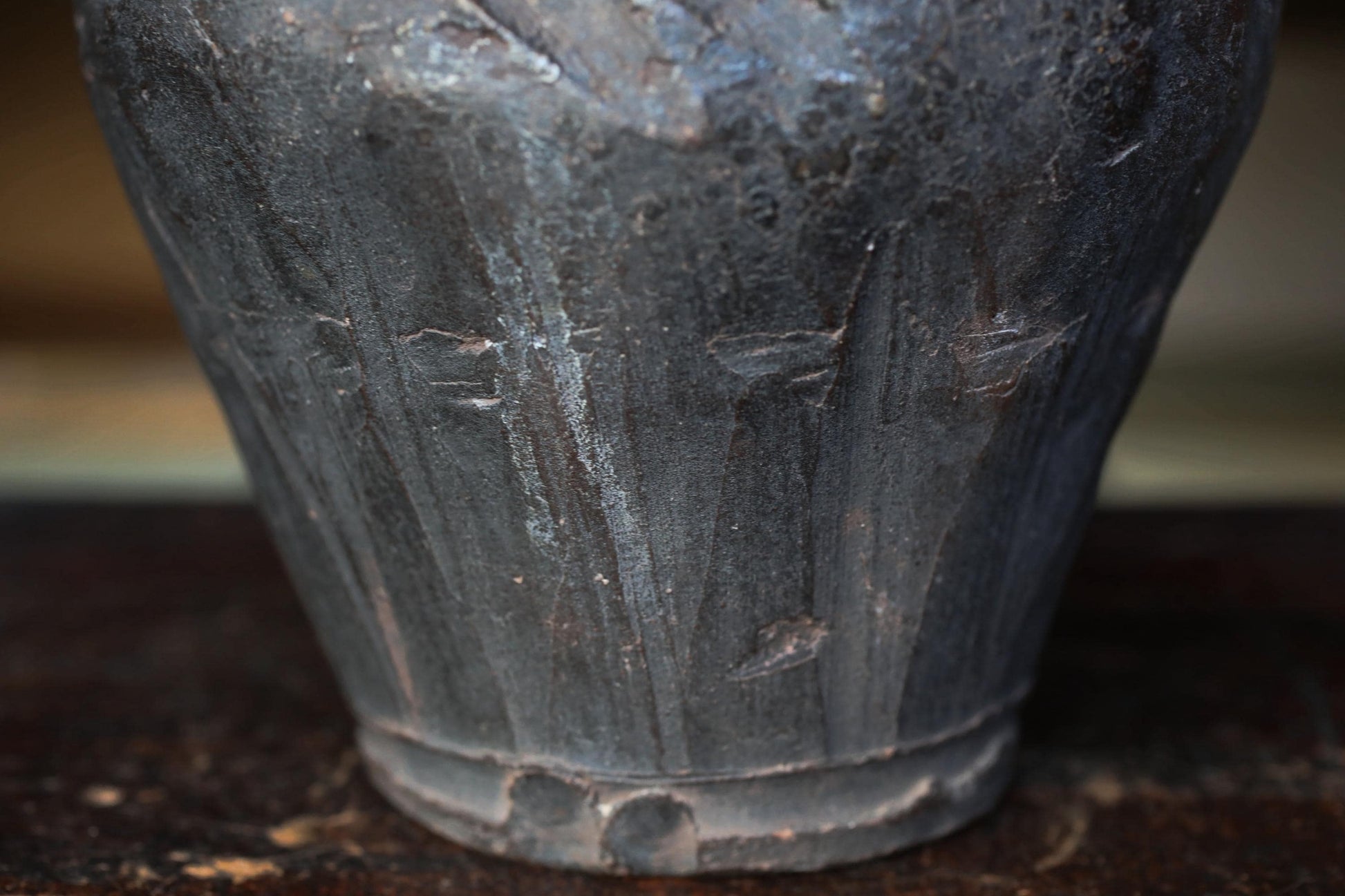 A close-up view of a dark, textured vase or container with a weathered appearance.