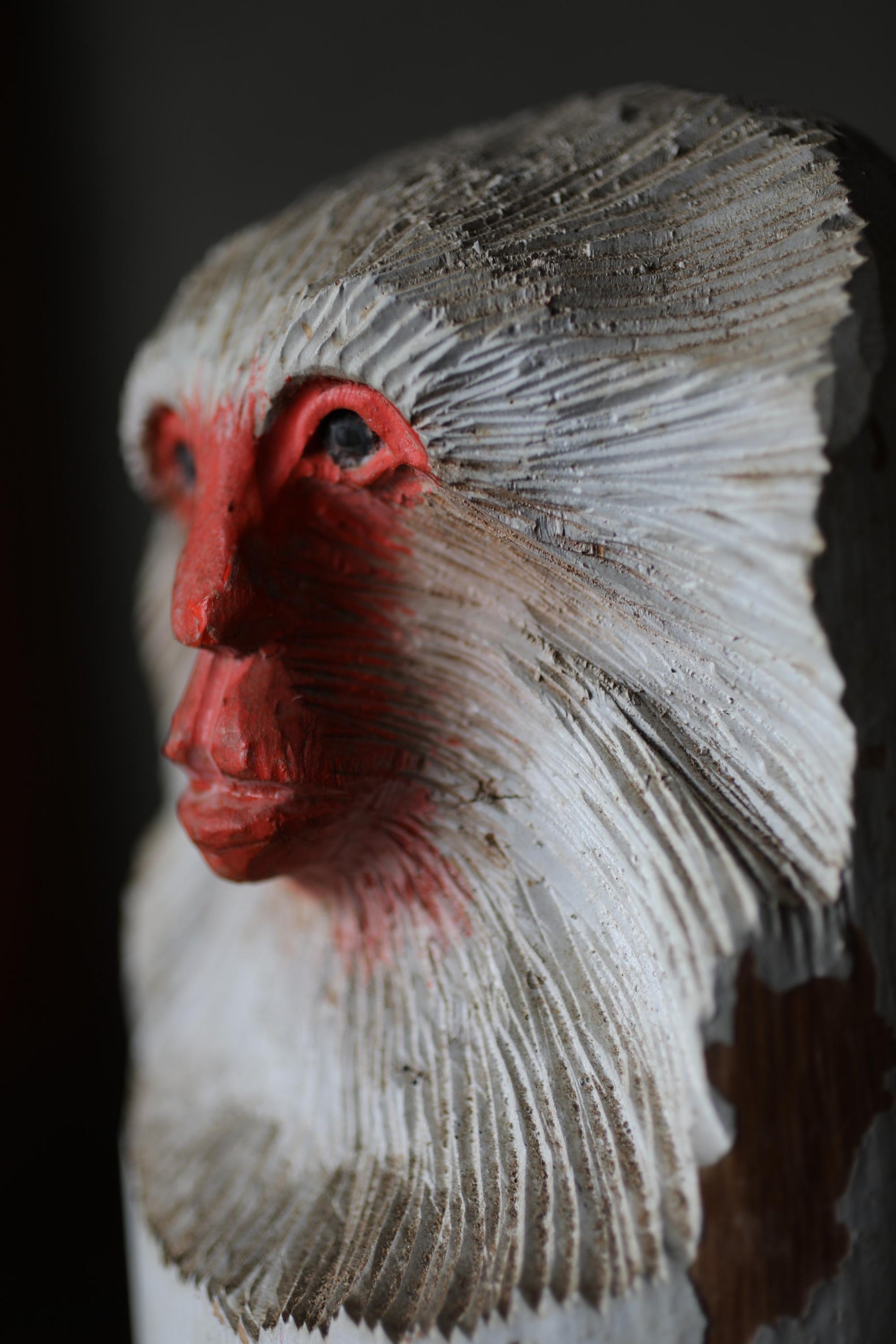 A close-up of a wooden sculpture depicting a monkey's face with a red nose and white fur.