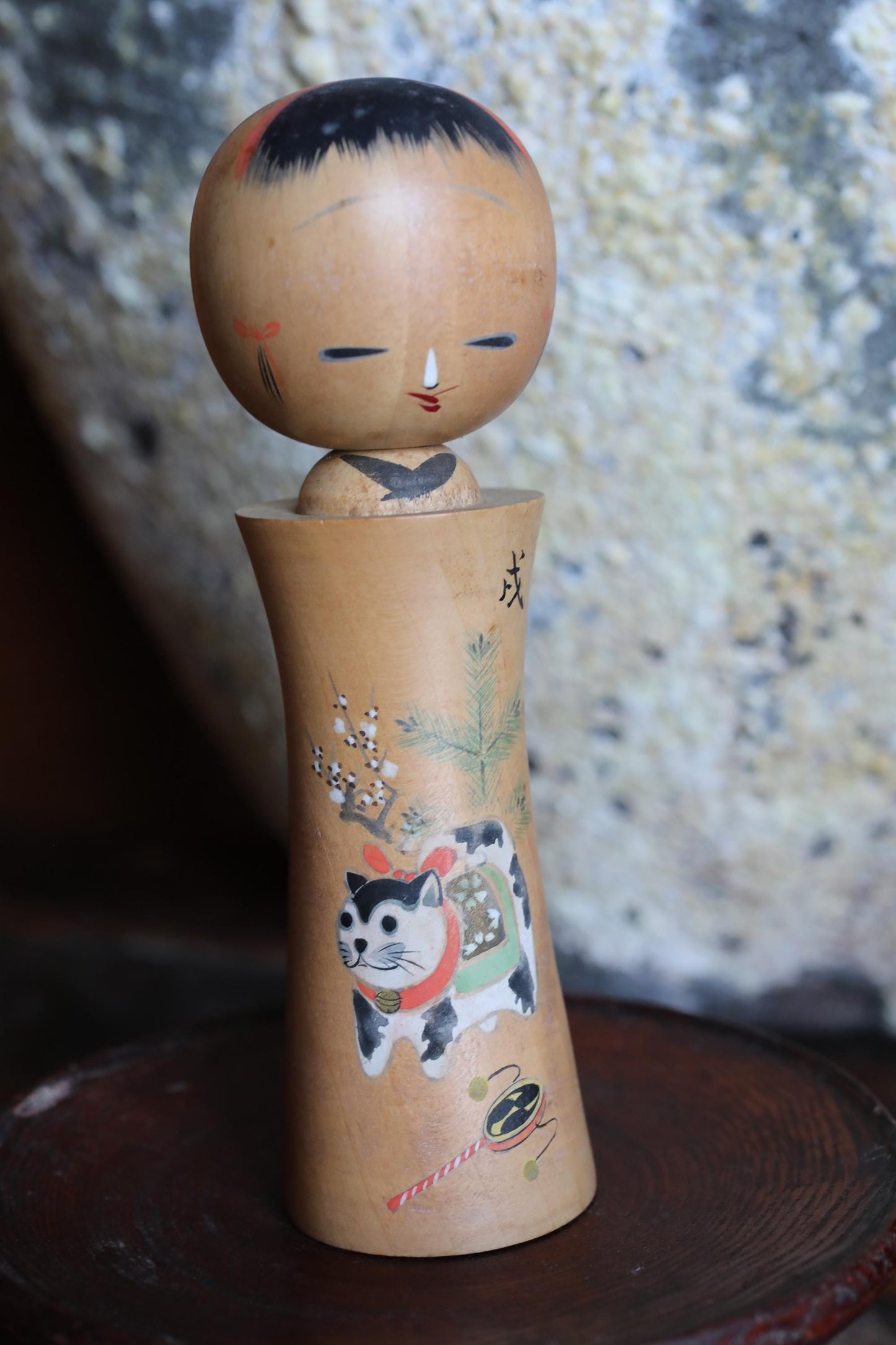 A wooden doll with a cat design on it, sitting on a wooden surface.