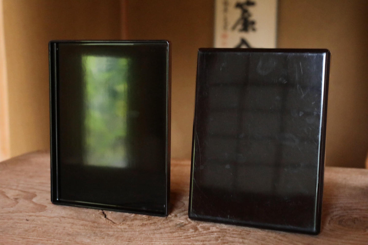 Two black rectangular objects are placed on a wooden surface, with a blurred background that includes some text.
