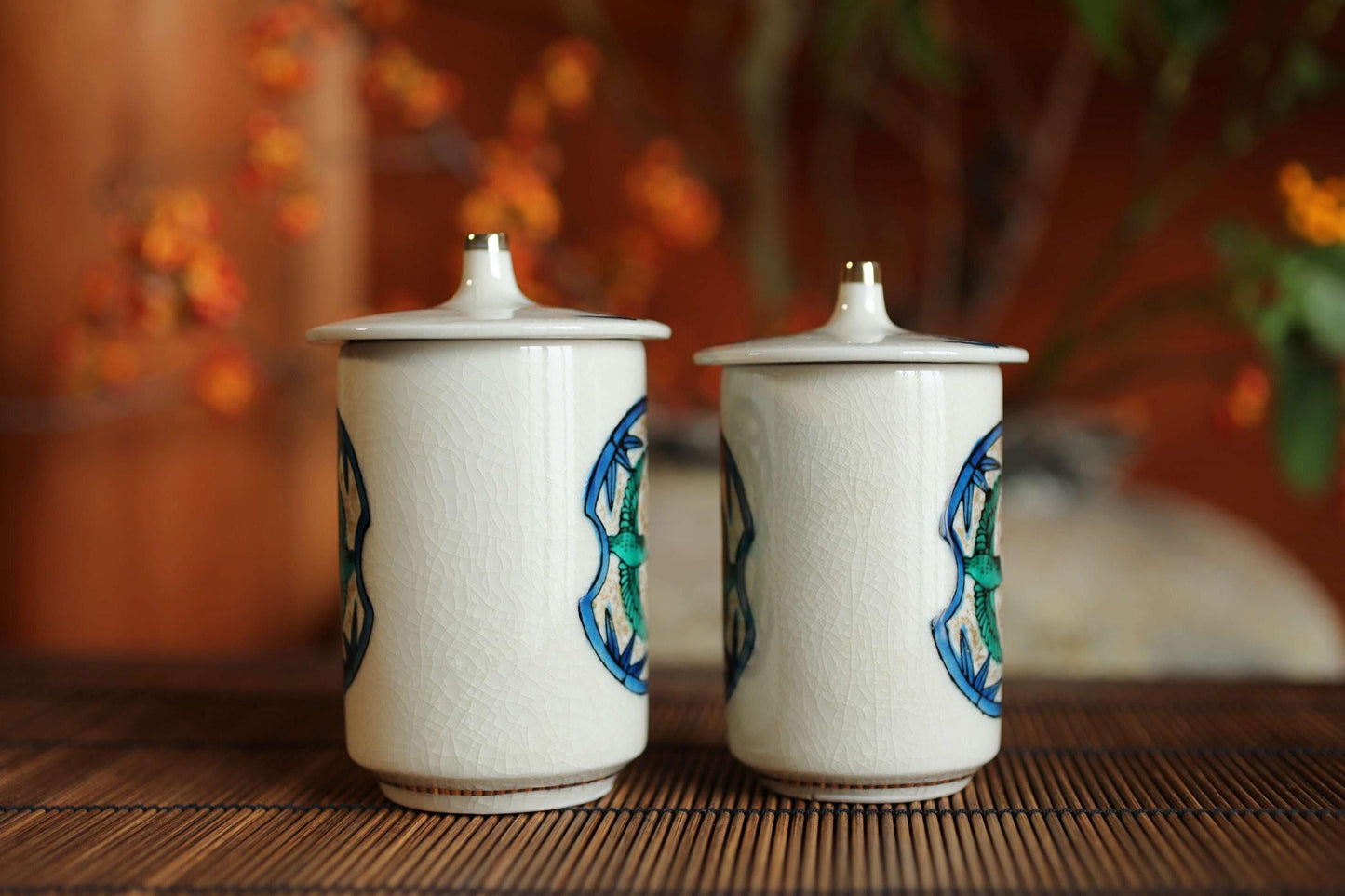 Two white ceramic containers with blue and green designs on them, placed on a wooden surface.