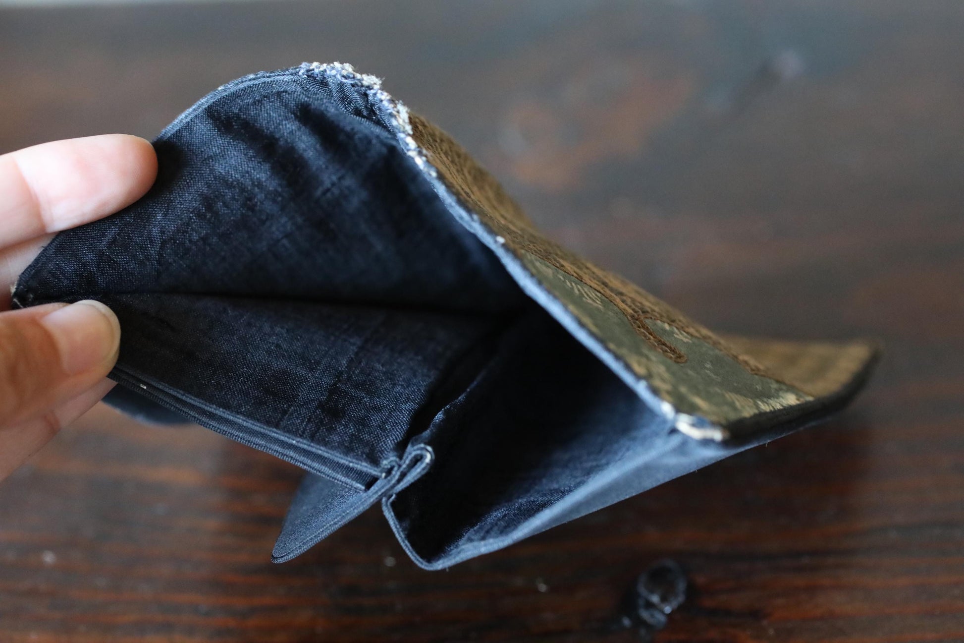 A hand is holding an open wallet with a black and brown patterned design on the flap.