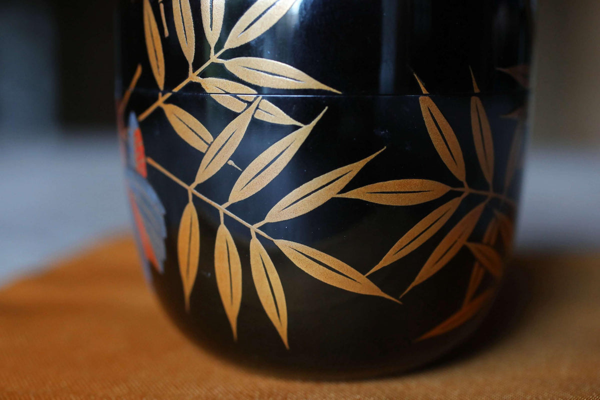 A close-up view of a black vase with gold leaf designs on it, placed on a wooden surface.