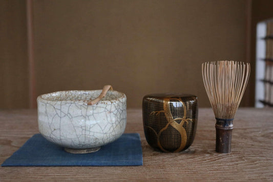 a variety of ceramic and wooden objects arranged on a wooden surface. There is a white ceramic bowl with a wooden spoon, a black ceramic container with a wooden handle, and a wooden whisk with a wooden handle.