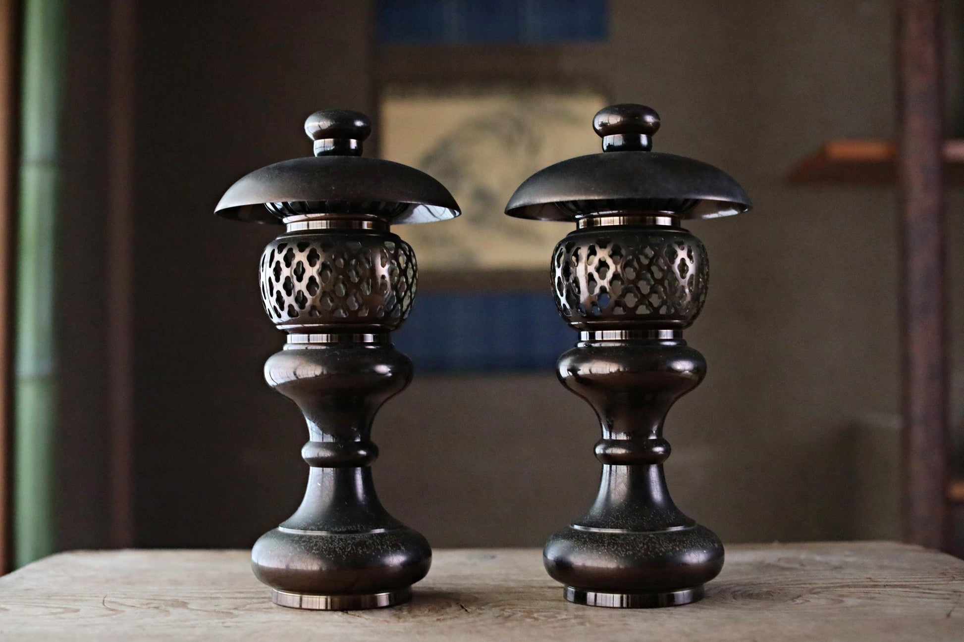 two ornate, black metal lanterns with intricate designs, placed side by side on a wooden surface.