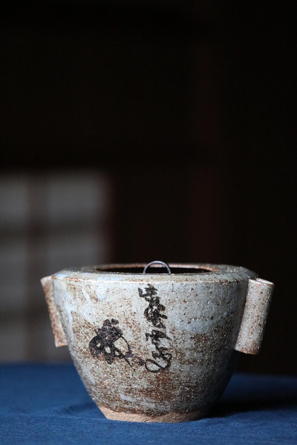 A white ceramic teapot with black text and designs on its surface, placed on a blue surface.