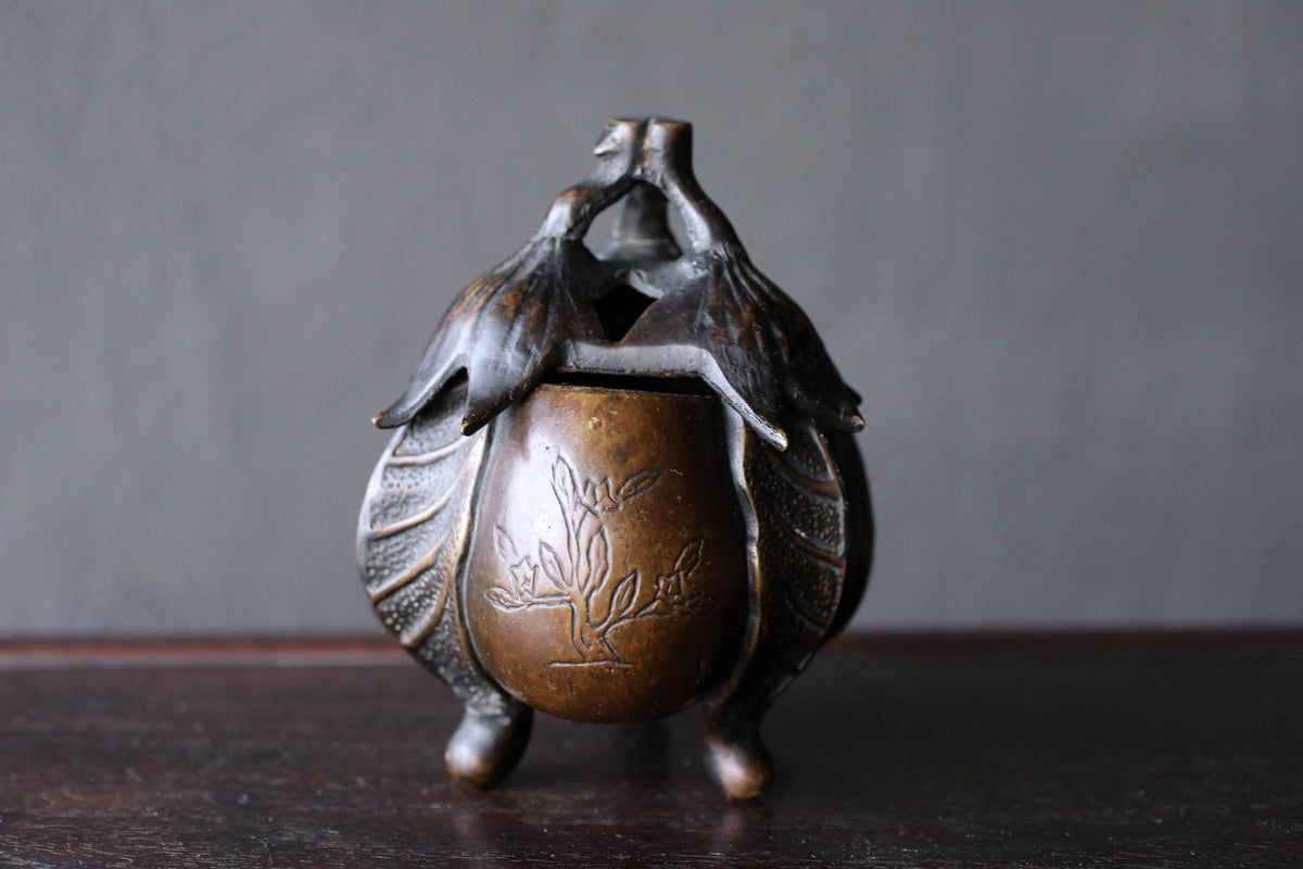 A bronze incense burner with a floral design on the front sits on a dark surface.