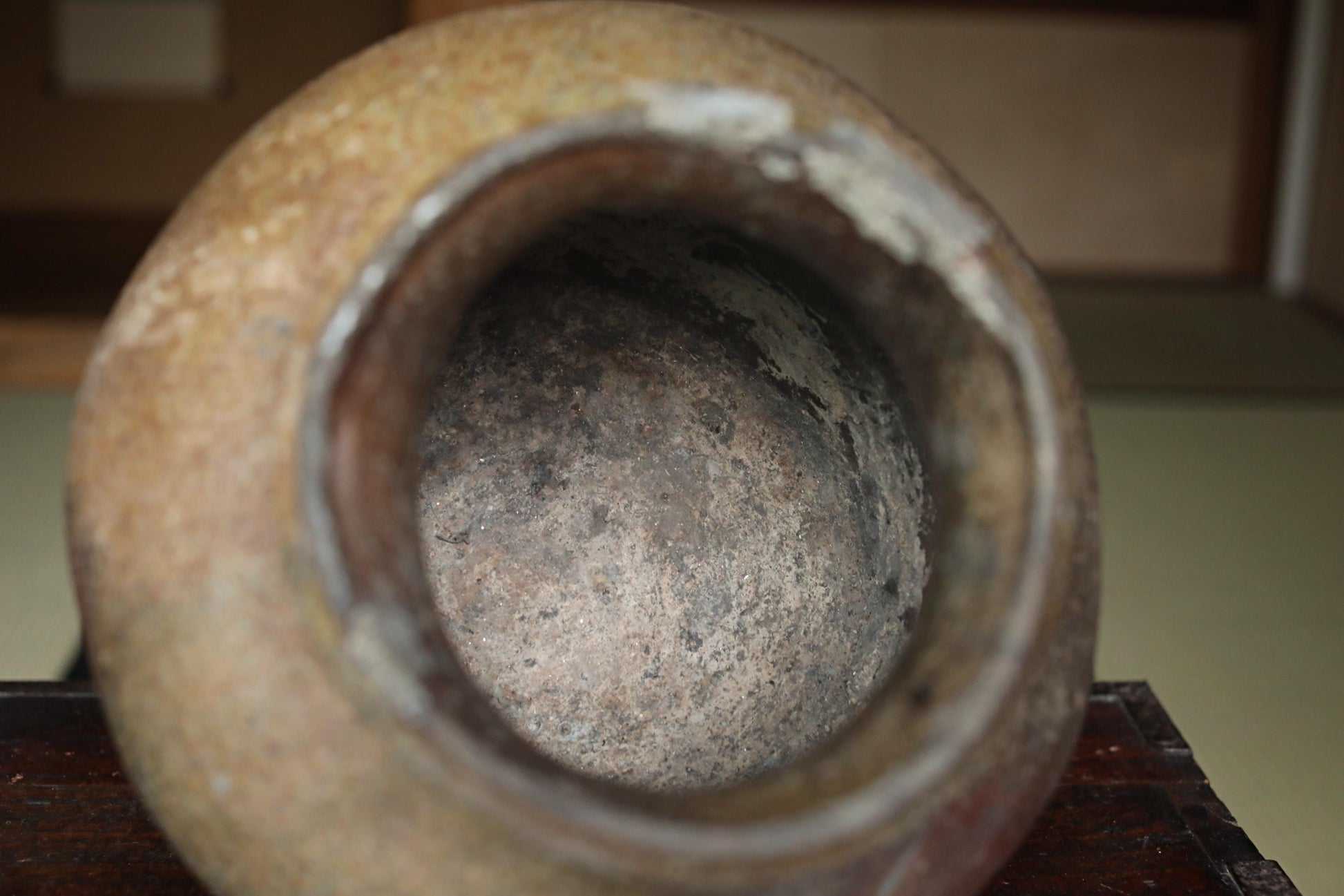 An old, rusted vase with a weathered, worn appearance sits on a wooden surface.