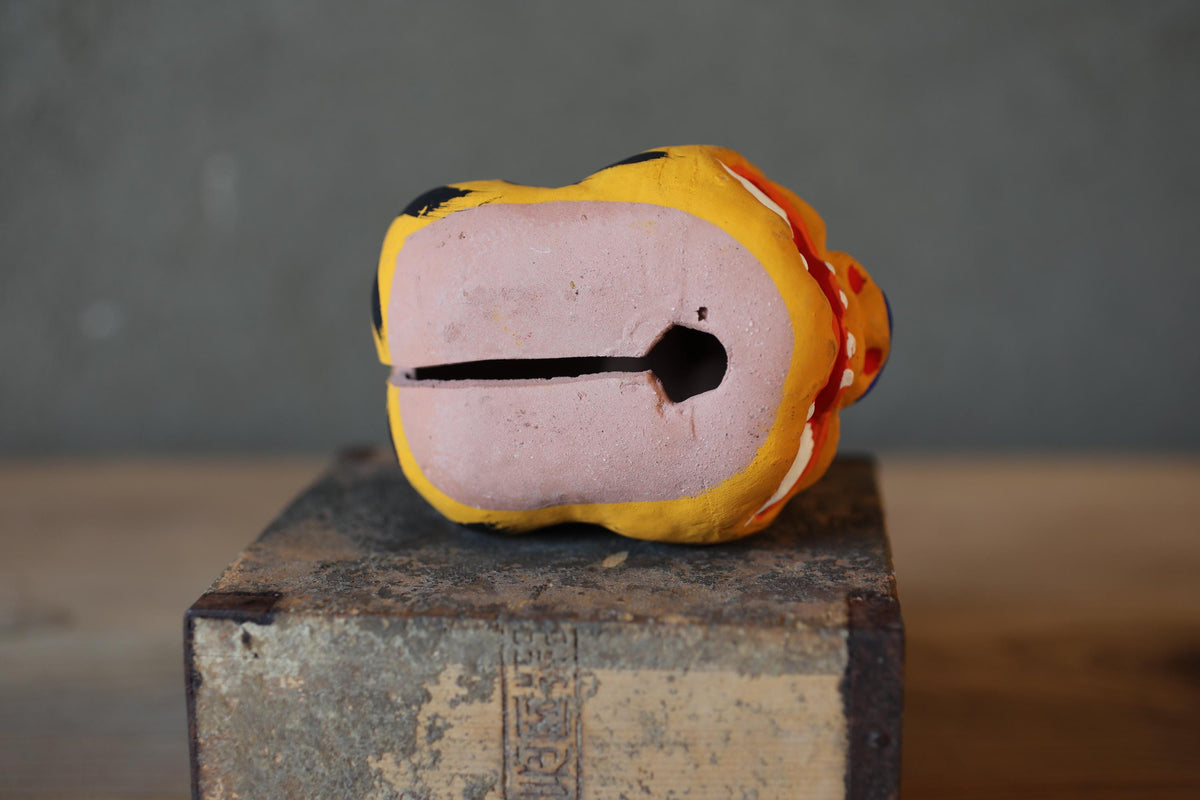 A colorful, hand-painted ceramic object resembling a small bird or frog sits on a wooden surface.