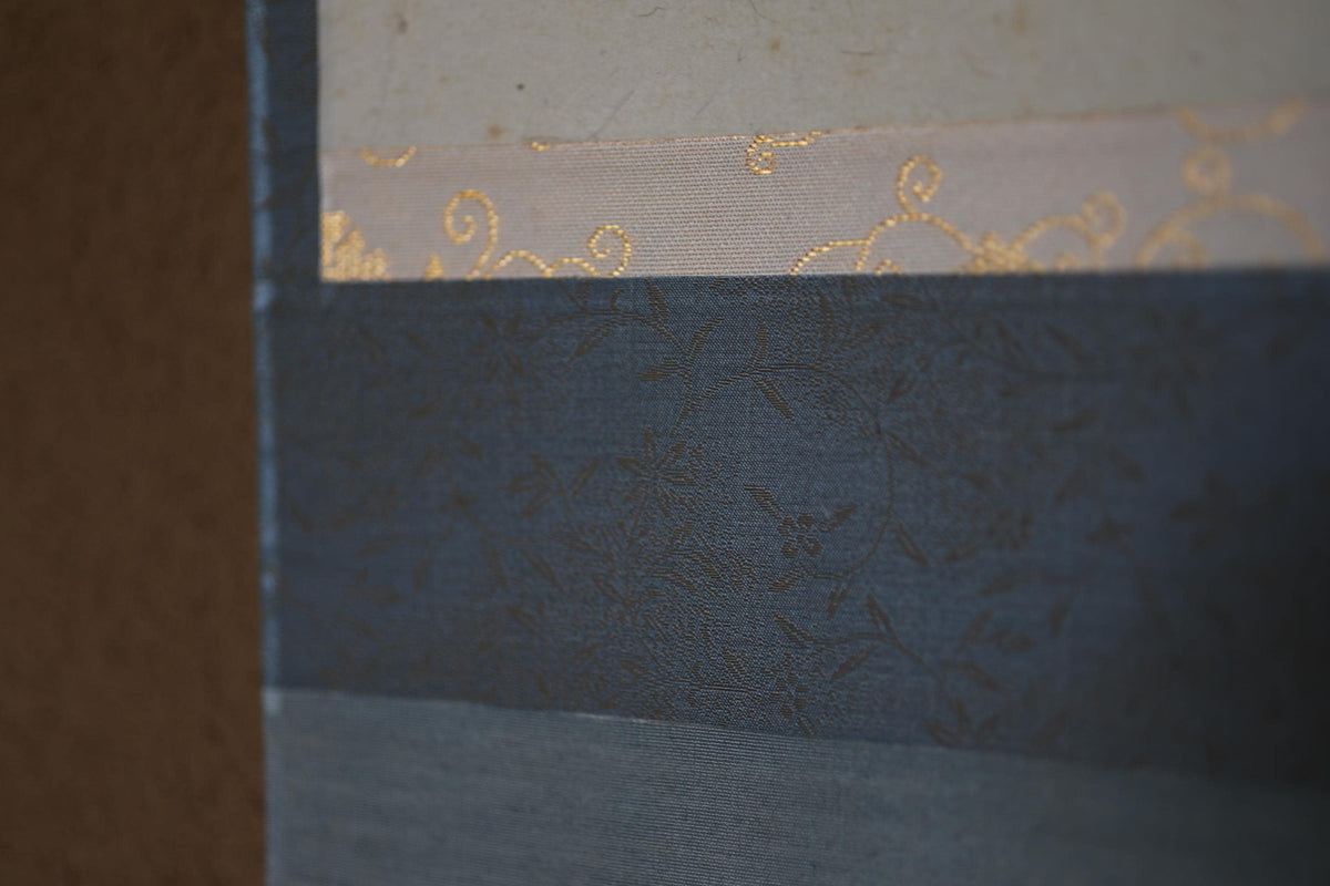 The image is a close-up of a textured fabric with a floral pattern, featuring a mix of blue, gray, and gold colors.