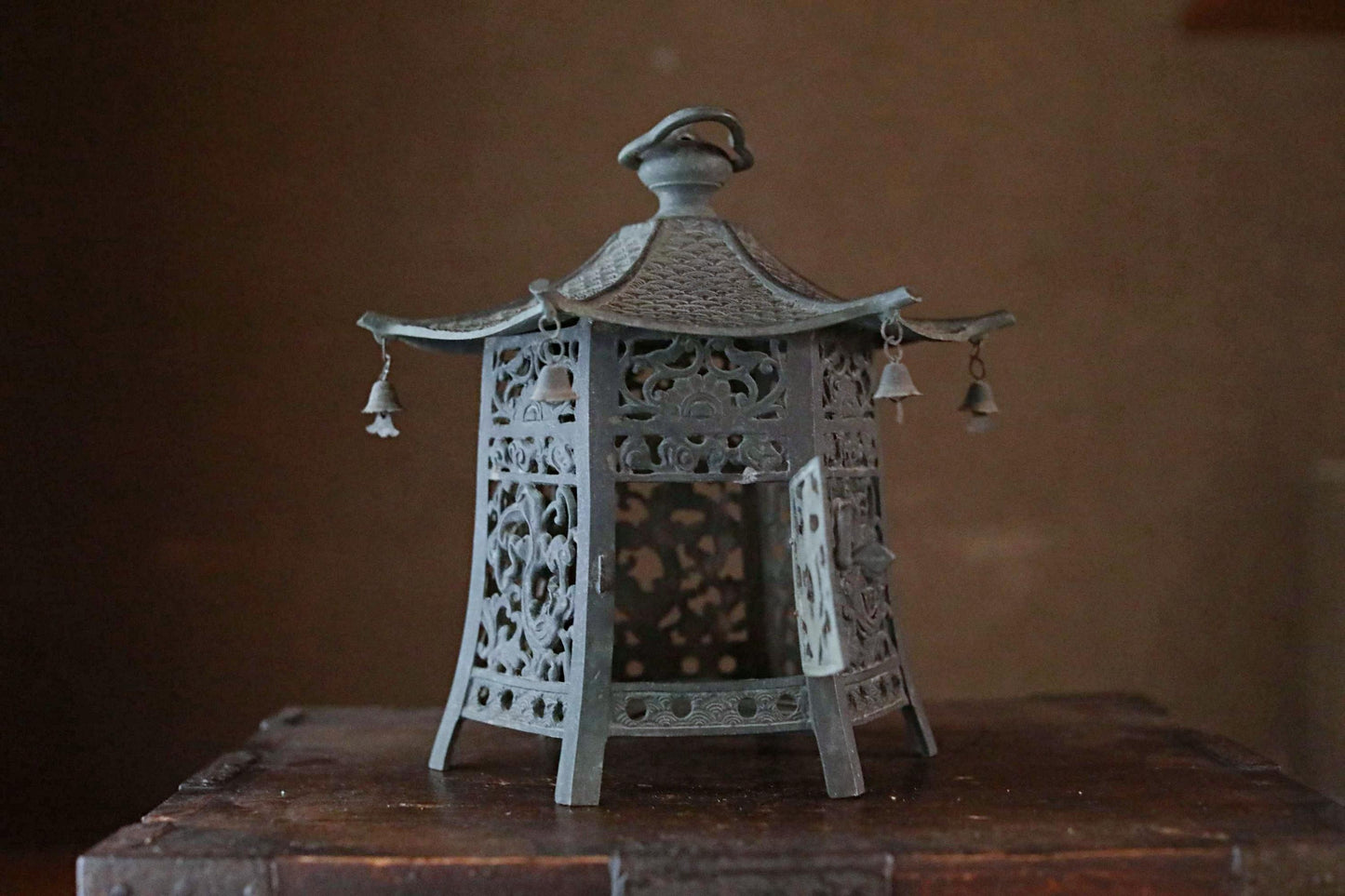 A decorative metal lantern with intricate designs and hanging bells, placed on a wooden surface.