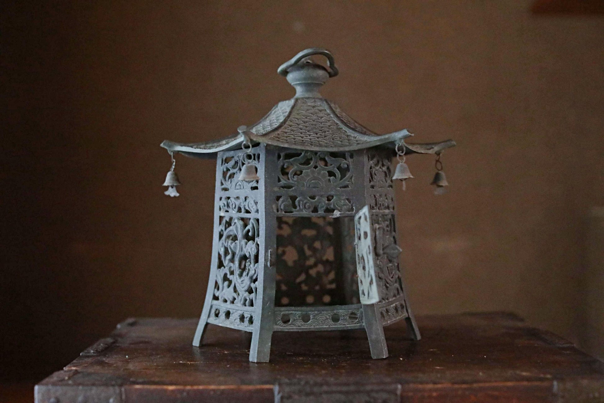 A decorative metal lantern with intricate designs and hanging bells, placed on a wooden surface.