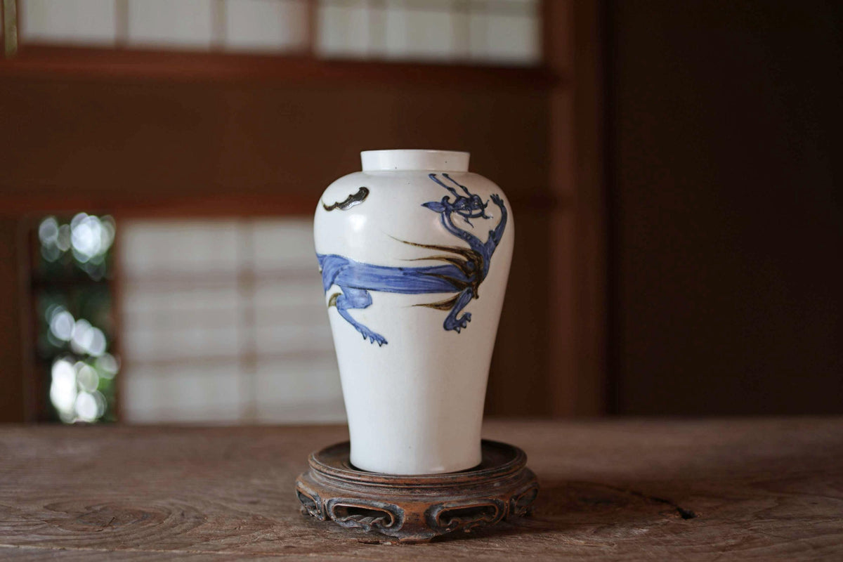 A white ceramic vase with a blue dragon design on it, placed on a wooden surface.