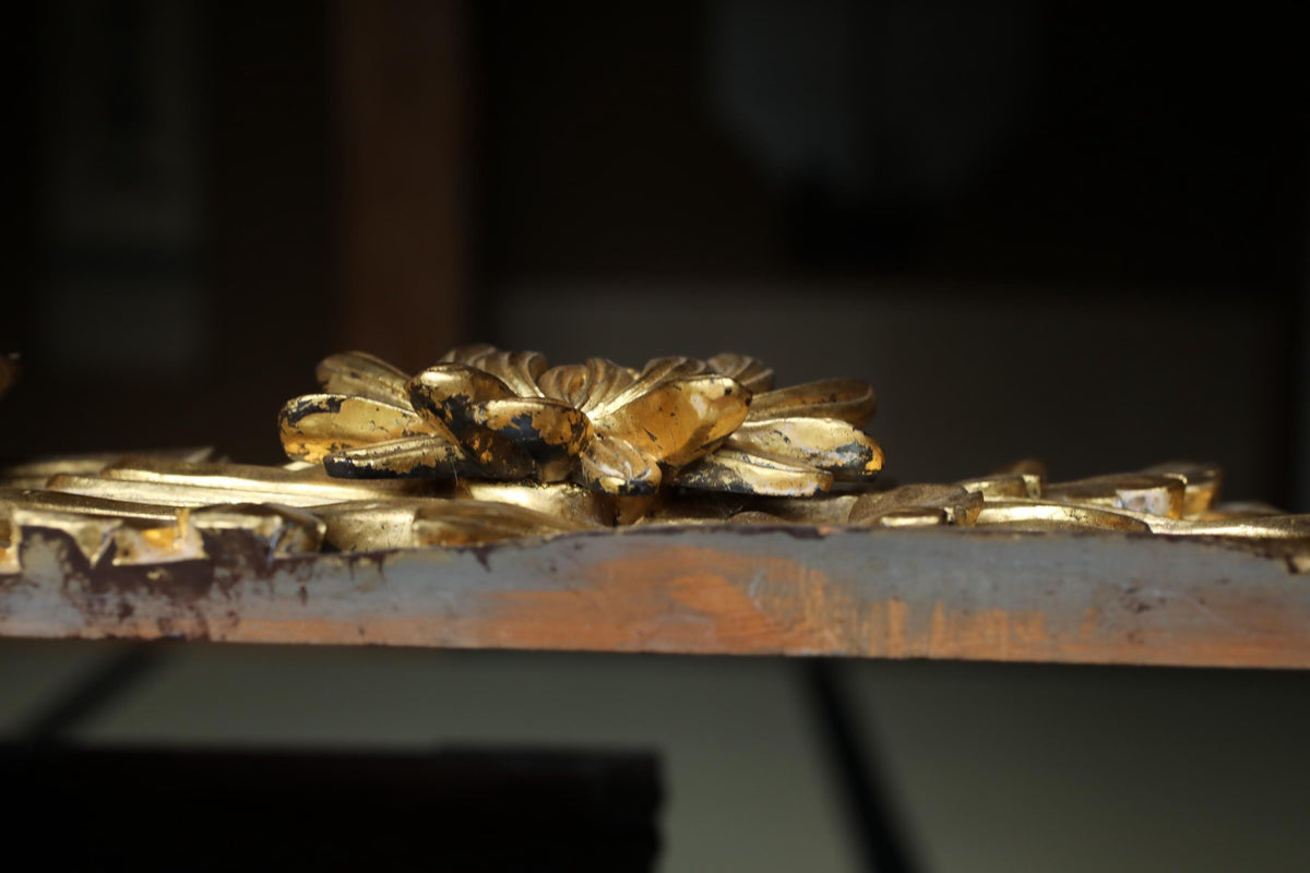 a close-up view of a golden, ornate object with intricate details, such as a flower or a decorative piece, resting on a wooden surface.