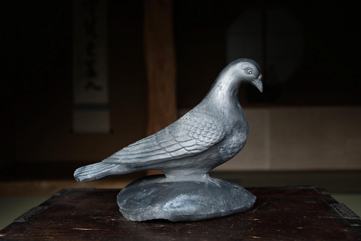 A silver metal bird statue is perched on a wooden surface.