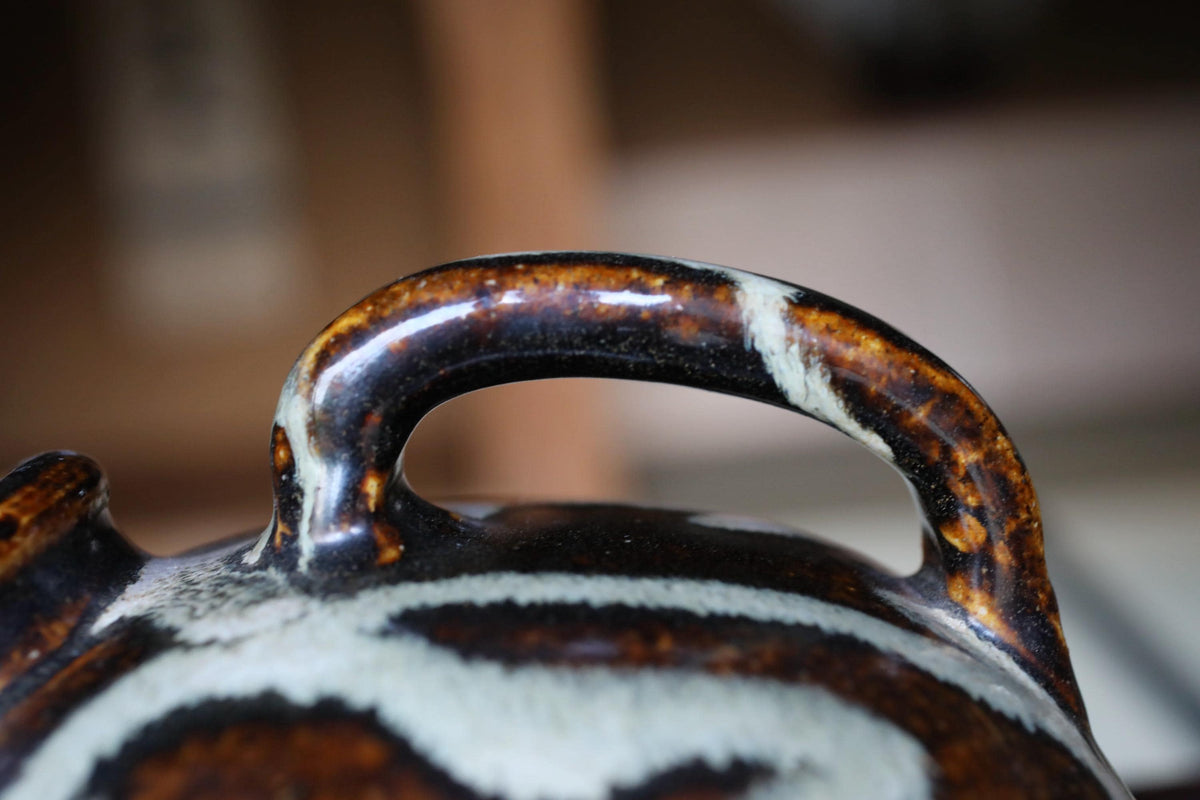 A close-up view of a ceramic handle or spout, with a dark brown and white patterned design.