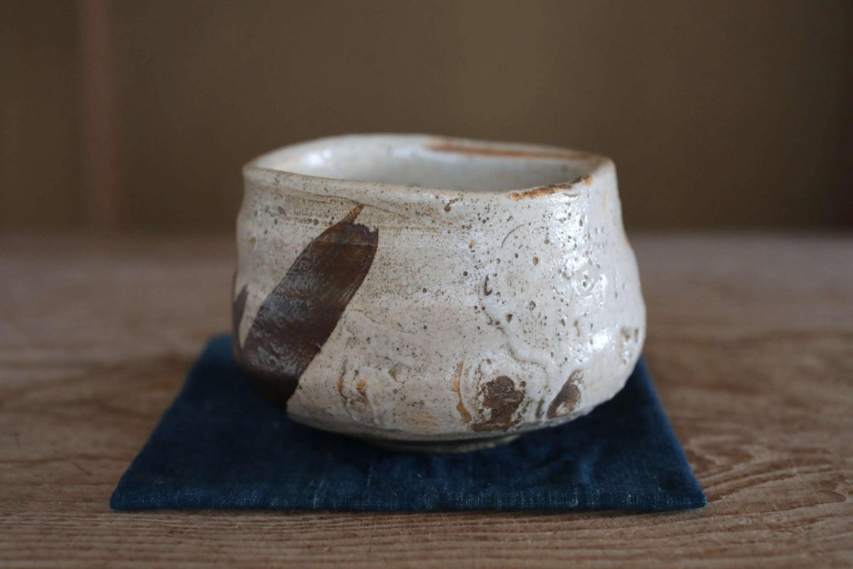 A white ceramic bowl with a brown design on it, placed on a blue cloth on a wooden surface.