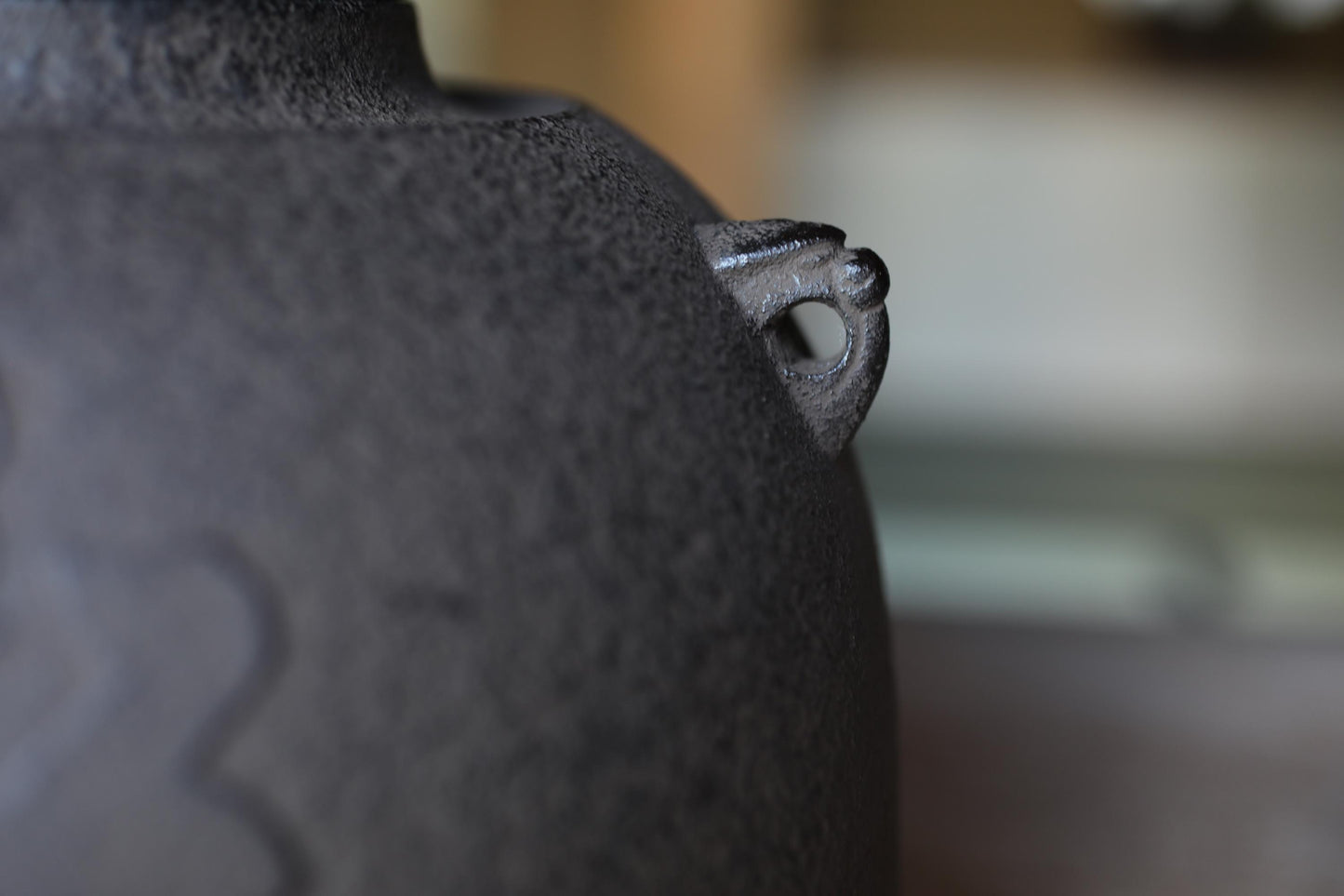 A close-up view of a dark-colored ceramic object, possibly a vase or bowl, with a small hole or opening on its side.