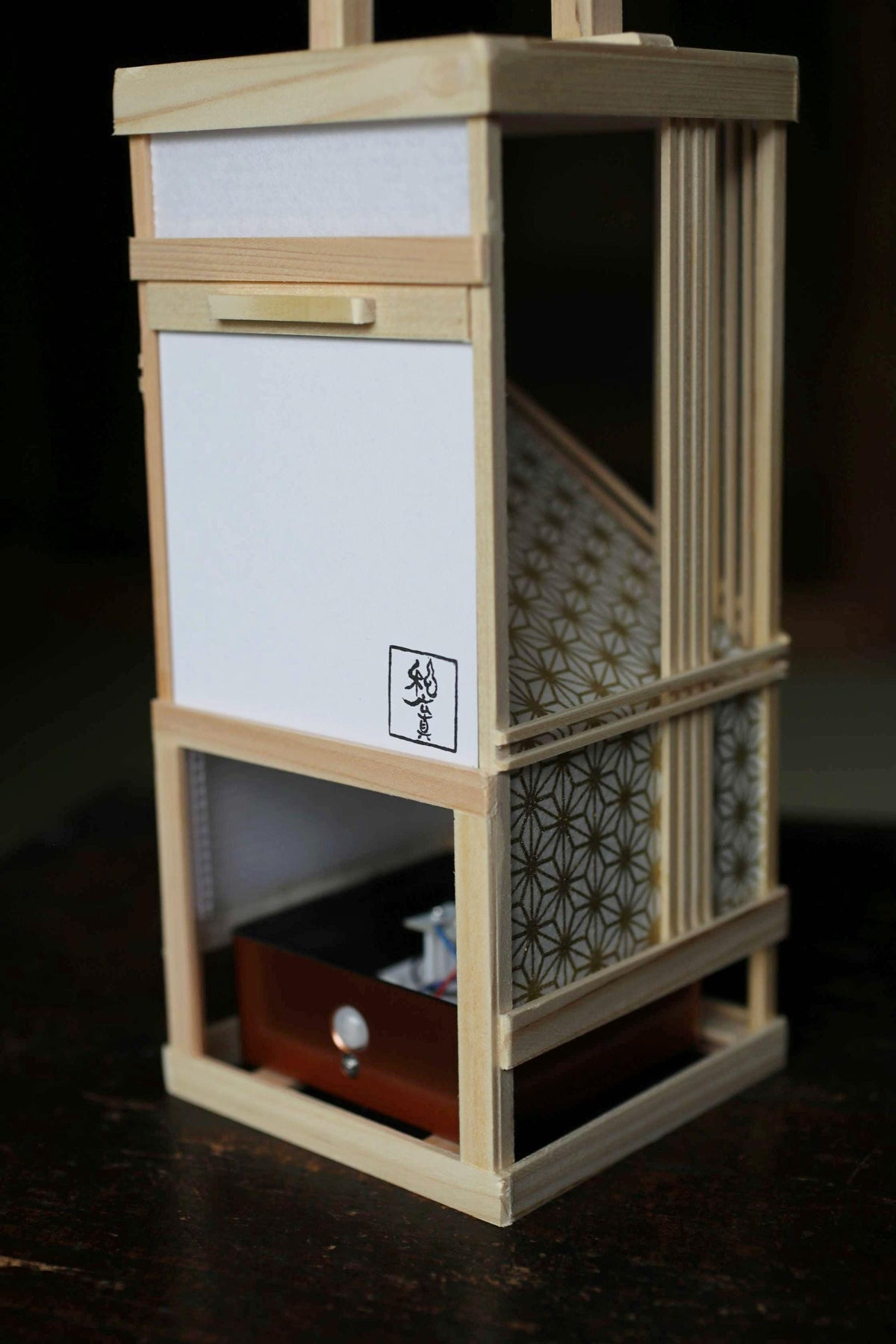 A wooden lantern with a white paper panel and a black and white patterned design on the front.