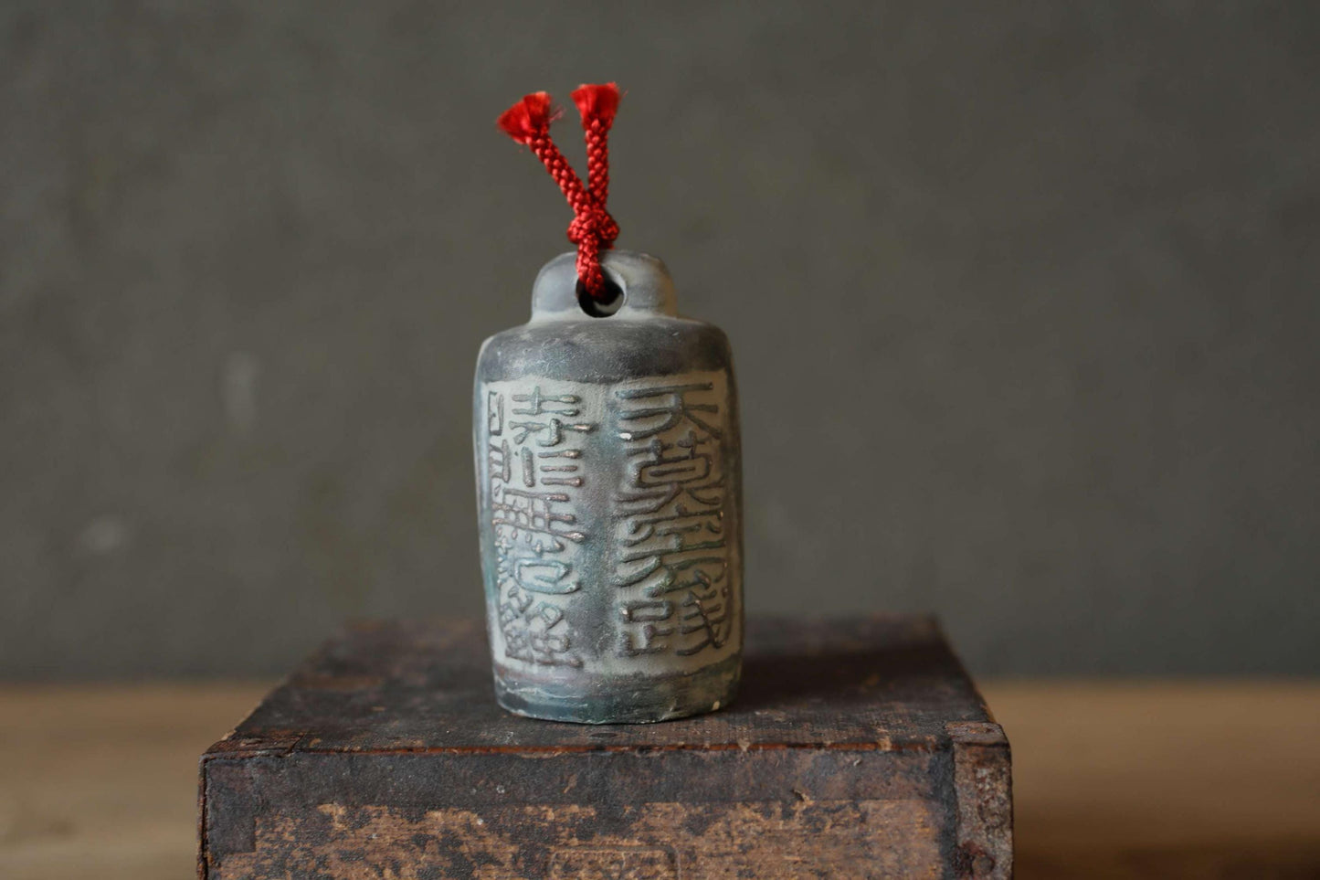 A ceramic bell with Chinese characters on it, placed on a wooden surface against a gray background.