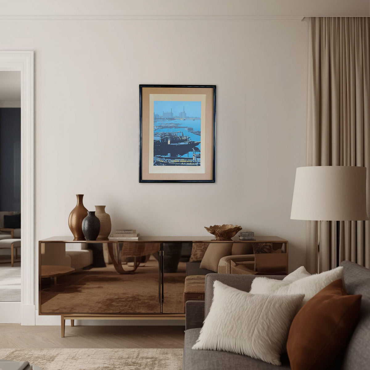 a living room with a framed picture of a ship hanging on the wall above a wooden console table. The console table has three vases and a lamp on it. The room also has a gray sofa with white pillows and a brown throw pillow.