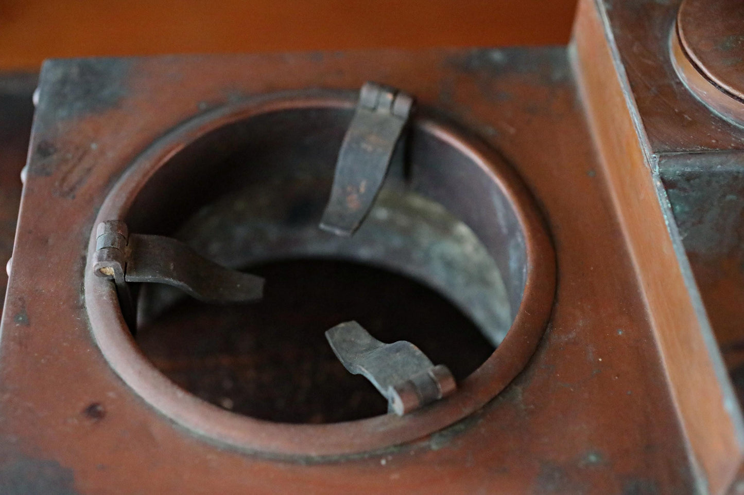 a close-up view of a metal container with a circular opening, featuring two metal hinges or clasps.