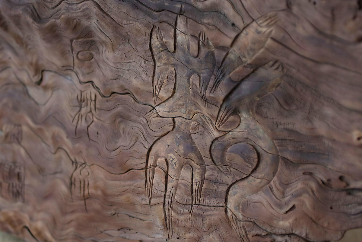 a close-up view of a wooden surface with intricate carvings and patterns, including a large, abstract design that appears to be a stylized representation of a bird or other organic shape.