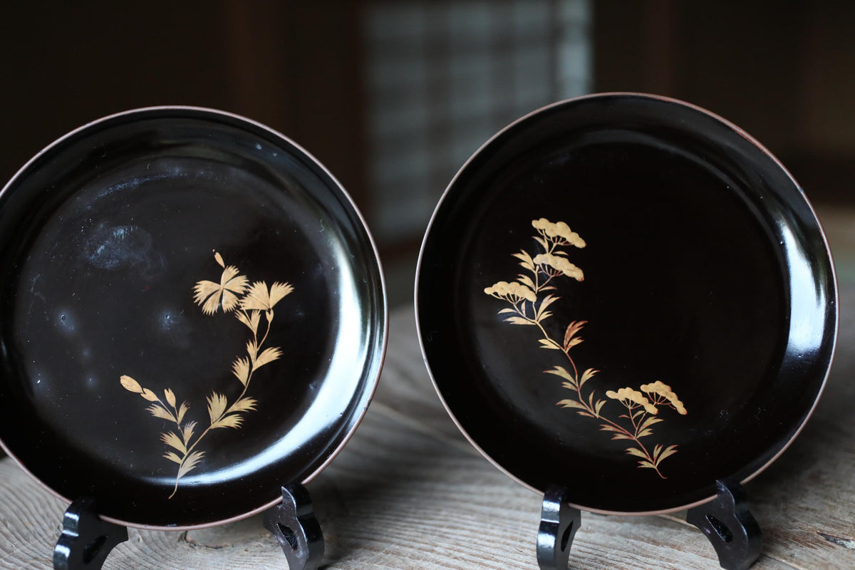 two black plates with gold floral designs on them, placed on a wooden surface.