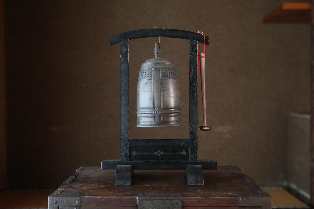 A silver bell is displayed on a black stand in a dimly lit room.
