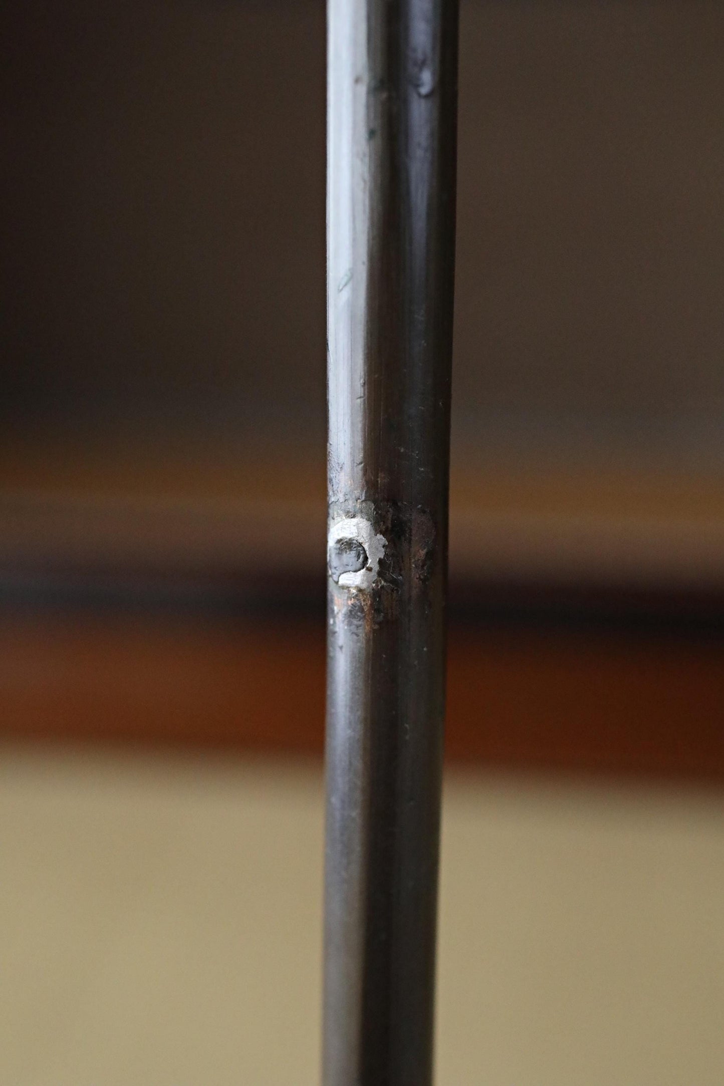 a close-up view of a metal pole or rod, with a small hole or puncture mark visible on its surface.