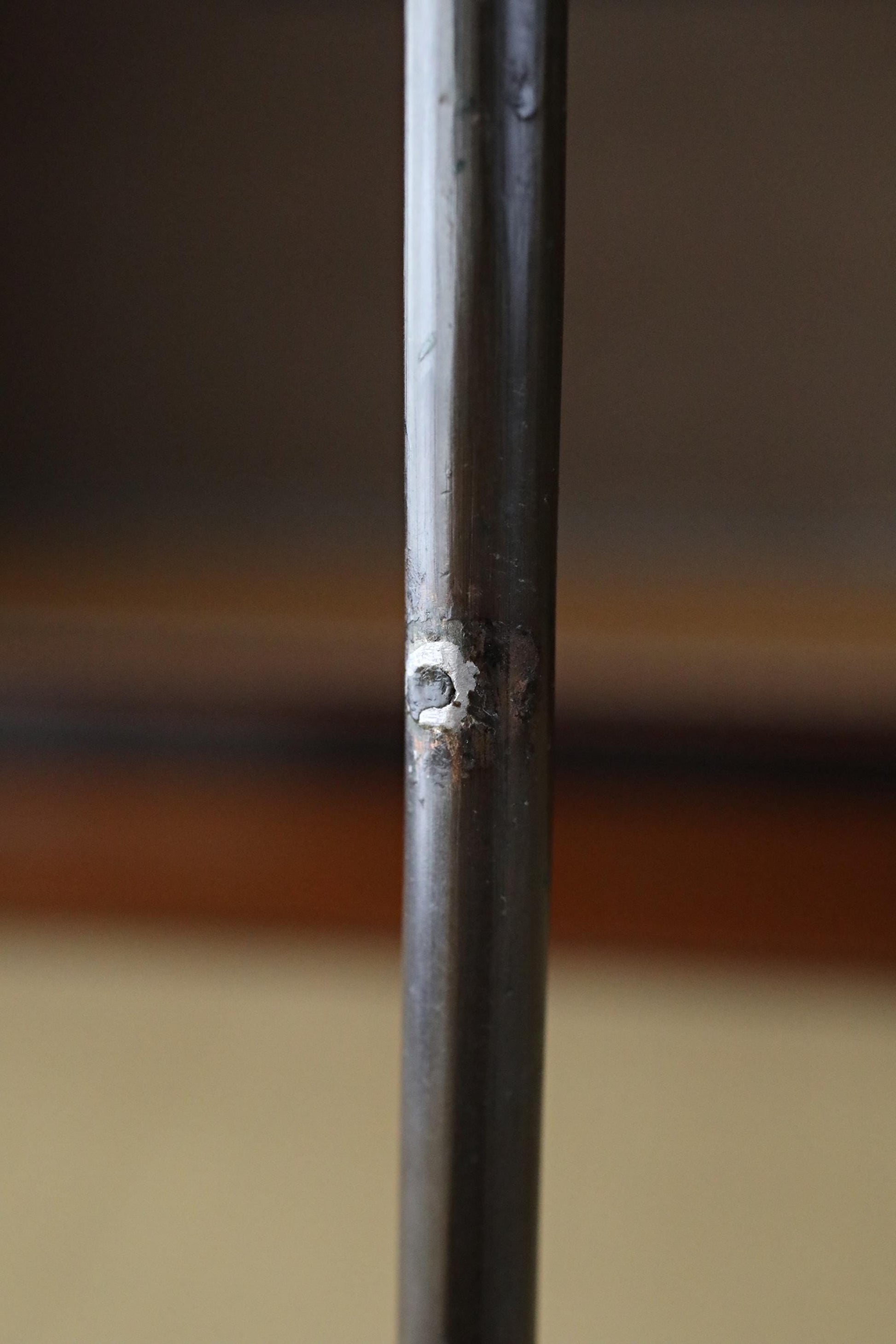 a close-up view of a metal pole or rod, with a small hole or puncture mark visible on its surface.