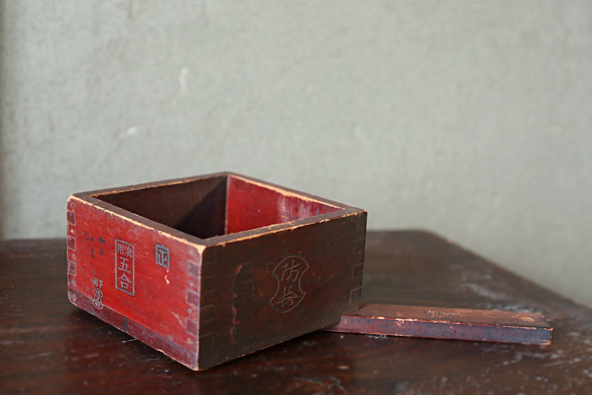 An old, weathered wooden box with a red exterior sits on a wooden surface, with a small piece of the box visible on the right side.