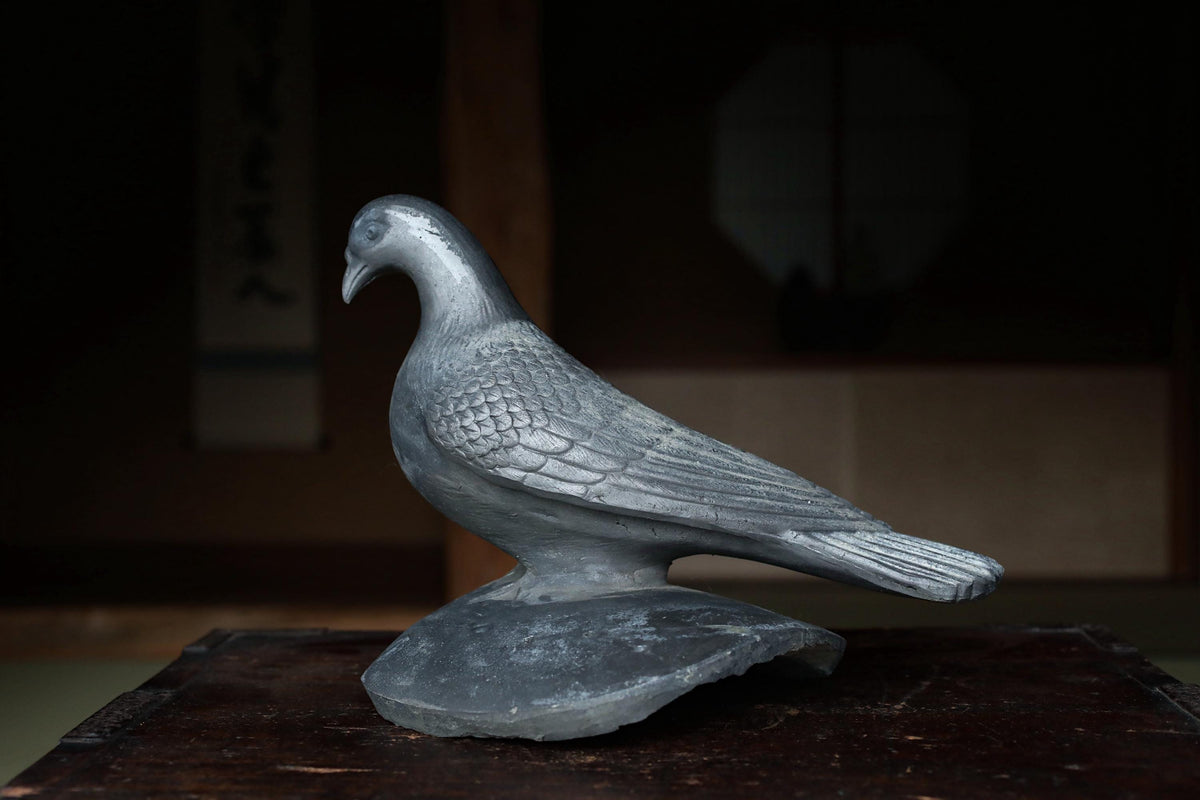 A silver metal bird statue is sitting on a wooden surface.