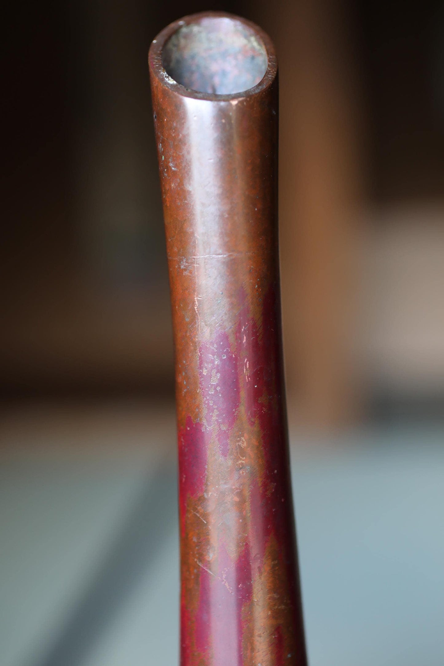 A close-up view of a rusted, metallic pipe or tube with a reddish-brown hue.