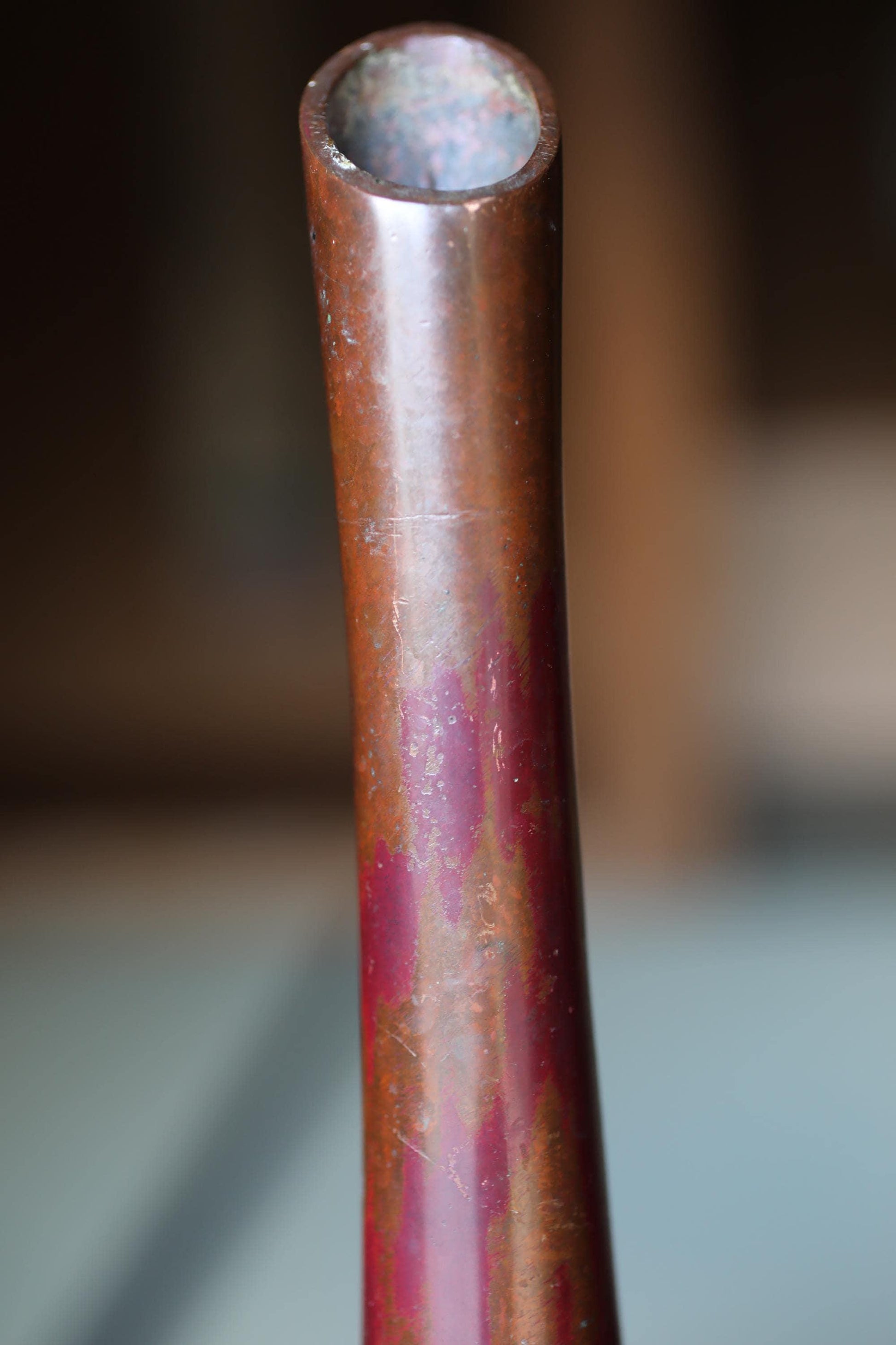 A close-up view of a rusted, metallic pipe or tube with a reddish-brown hue.