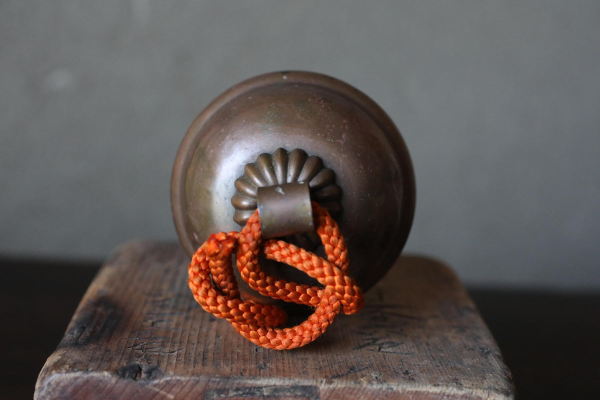 A round, brown bell with a red rope attached to it, placed on a wooden surface.