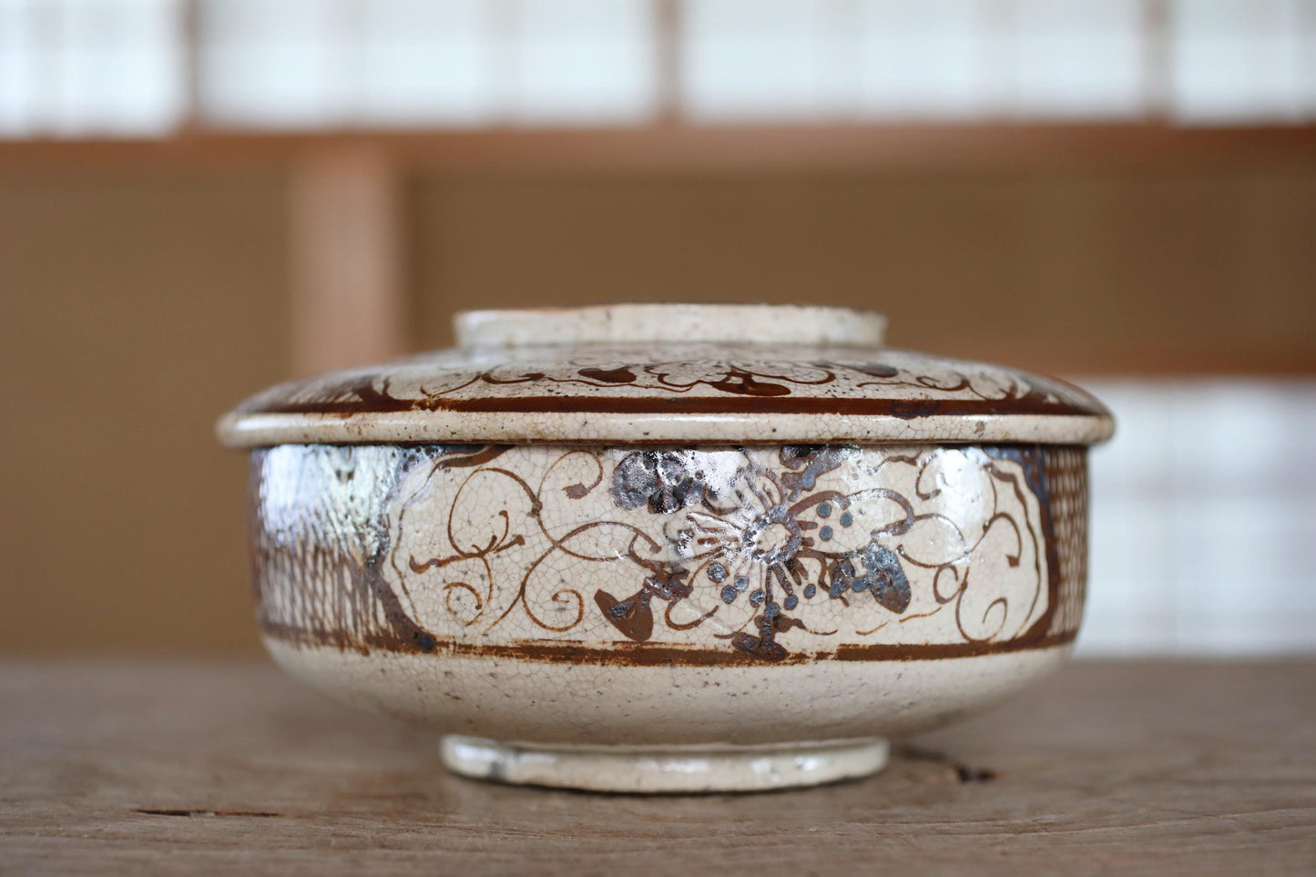 A decorative ceramic bowl with a floral pattern sits on a wooden surface.