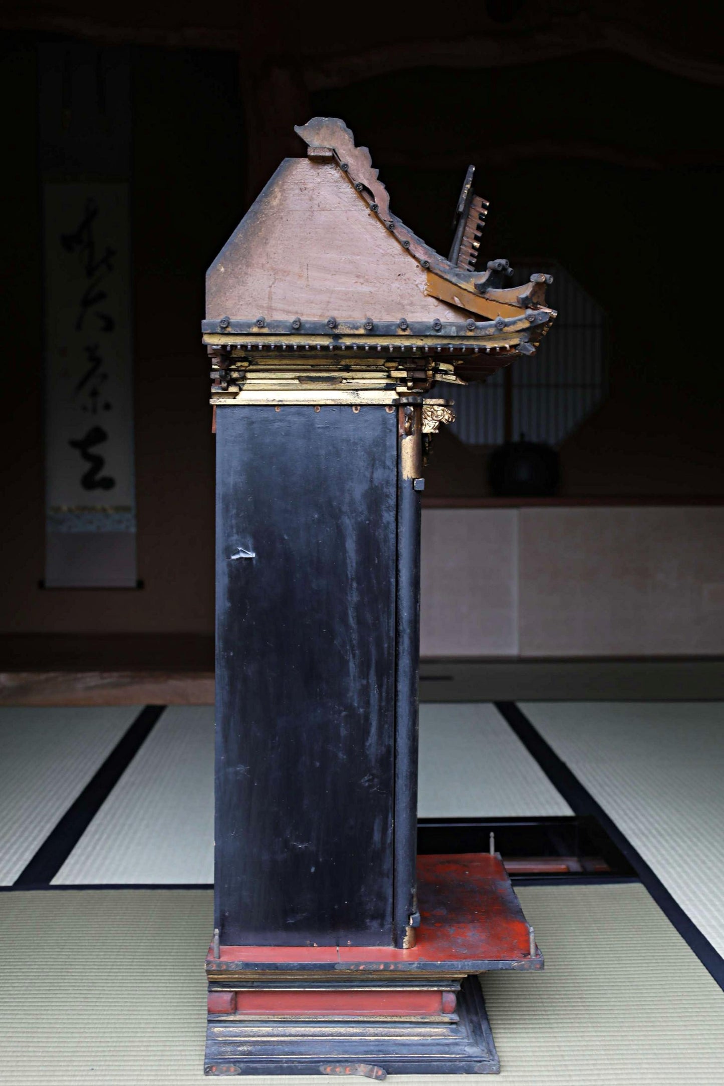 a black and red wooden structure with a pointed roof, standing on a tatami mat.